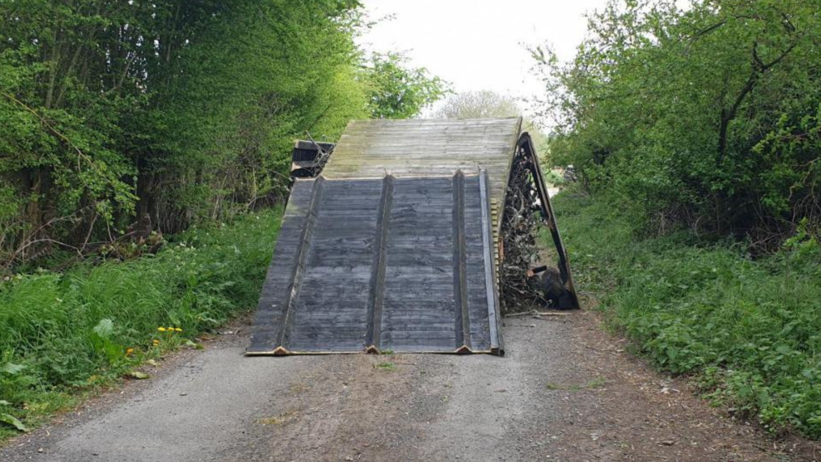 A photo of the fly-tip on Monument Road in which you can see large fences stacked up against tree cuttings in the middle of the road