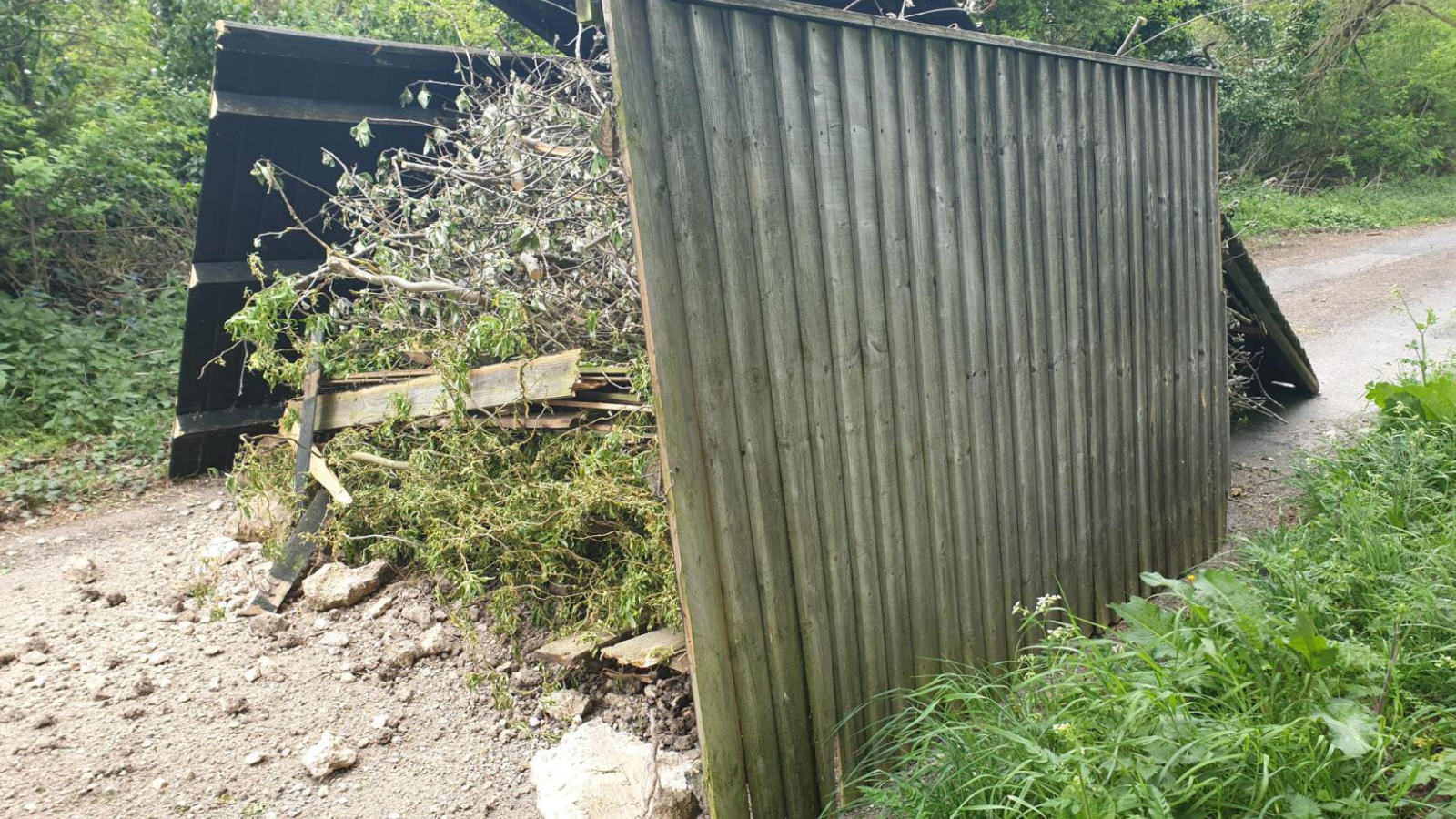 A photo of the fly-tip on Monument Road in which you can see large fences stacked up against tree cuttings in the middle of the road