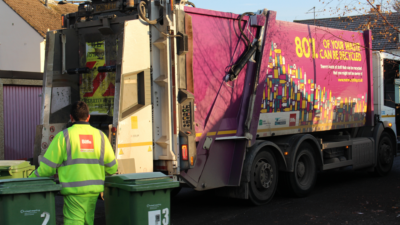 A photo of a binman pulling two bins to a waste and recycling trucks